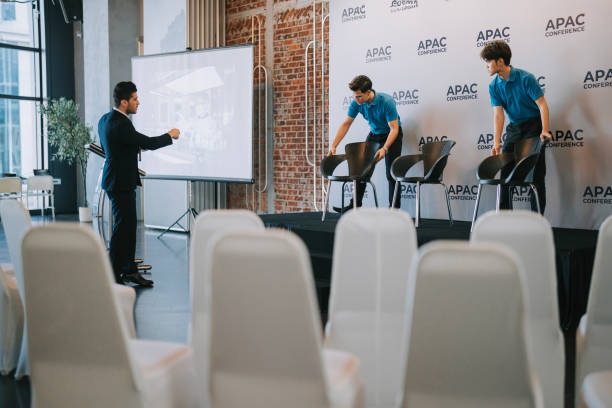 istock Asian Banquet hall manager coordinating crew arranging VIP speaker seat on stage before the business conference seminar begin 1580743104