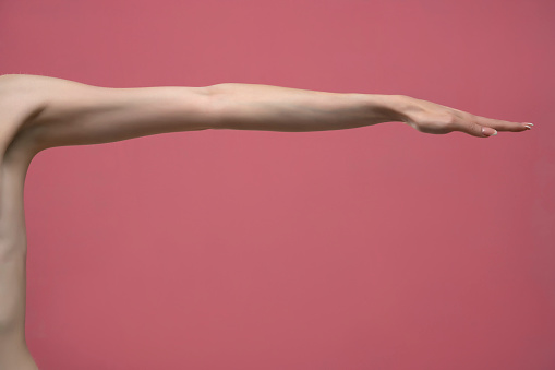 Young woman's stretched arm and palm. Isolated on pink background