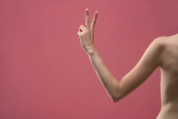 2本の指を示す若い女性の腕。ピンクの背景に分離型 - arm slim ストックフォトと画像