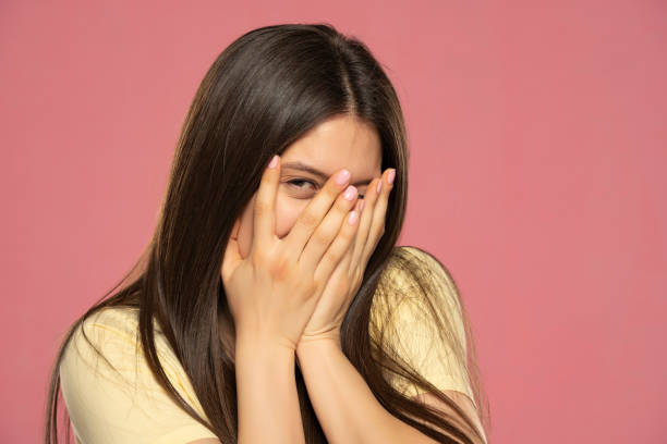 istock beautiful young female peeks though fingers, covers face with both hands, has shy expression 1580773523