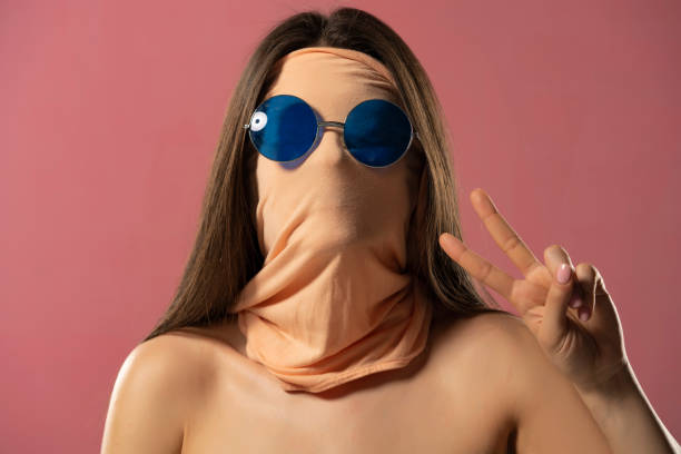 portrait of unknown woman with face wrapped in fabric wearing glasses and showing two fingers on a pink colour background - blank expression head and shoulders horizontal studio shot imagens e fotografias de stock