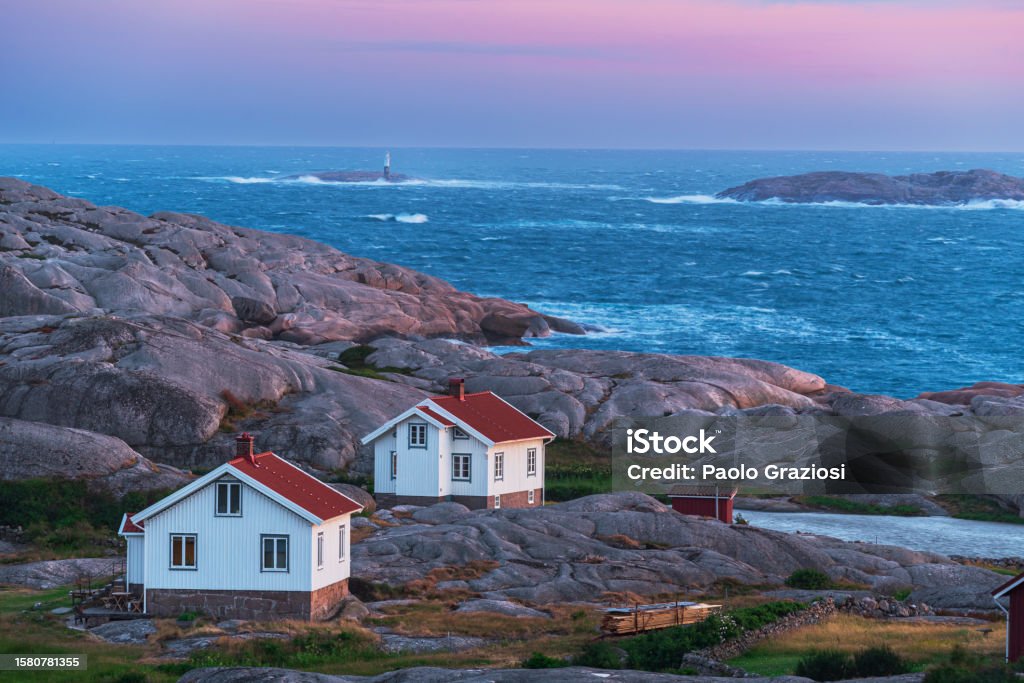 Isolated houses in the rocky and wild landscape surrounded rough sea Isolated white painted cottage in the dramatic landscape by the sea at dusk, Ramsvik island, Bohuslan, Sweden, Scandinavia Bohuslan Stock Photo