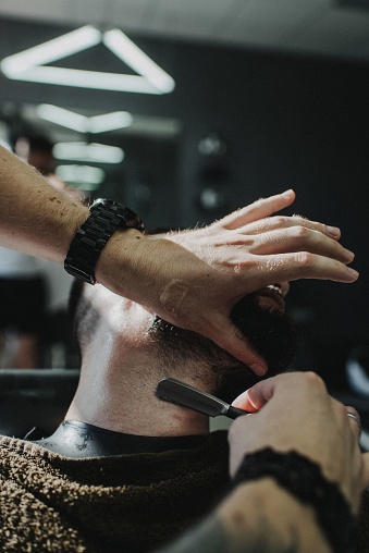 A skilled barber is meticulously styling the beard of a content customer in a barber's chair