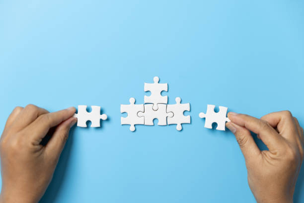 istock Two hands trying to connect couple puzzle piece on blue background. Teamwork concept. Closeup hand of connecting jigsaw puzzle. 1580782220