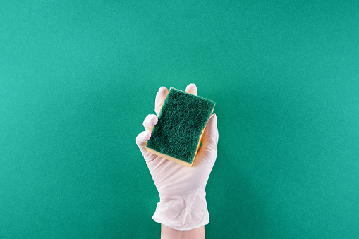 Hand Keeping Cleaning Sponge Over Green Background