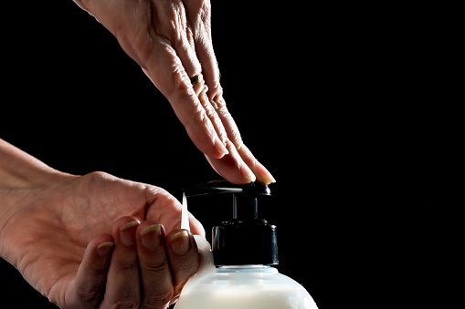 A closeup of the hands of a person putting hand cream on one hand on the black background