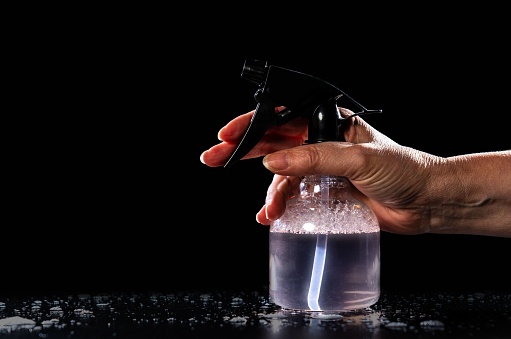 A closeup of a hand of a person holding a spray bottle on the black background