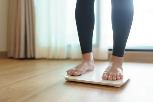 istock Lose weight. Fat diet and scale feet standing on electronic scales for weight control. Measurement instrument in kilogram for diet. 1580791088