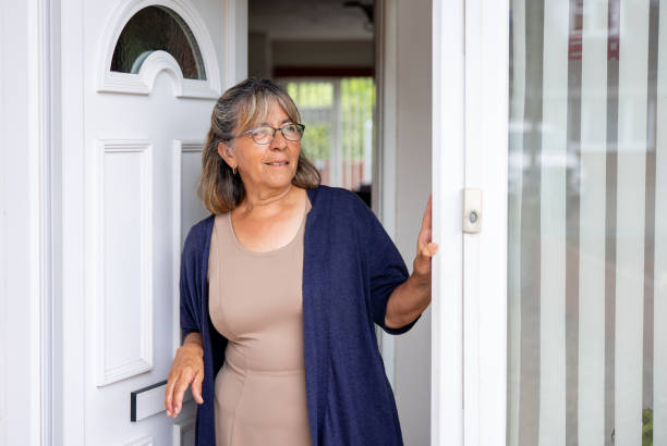 femme debout à la porte de sa maison et regardant ailleurs - nosy door women senior adult photos et images de collection