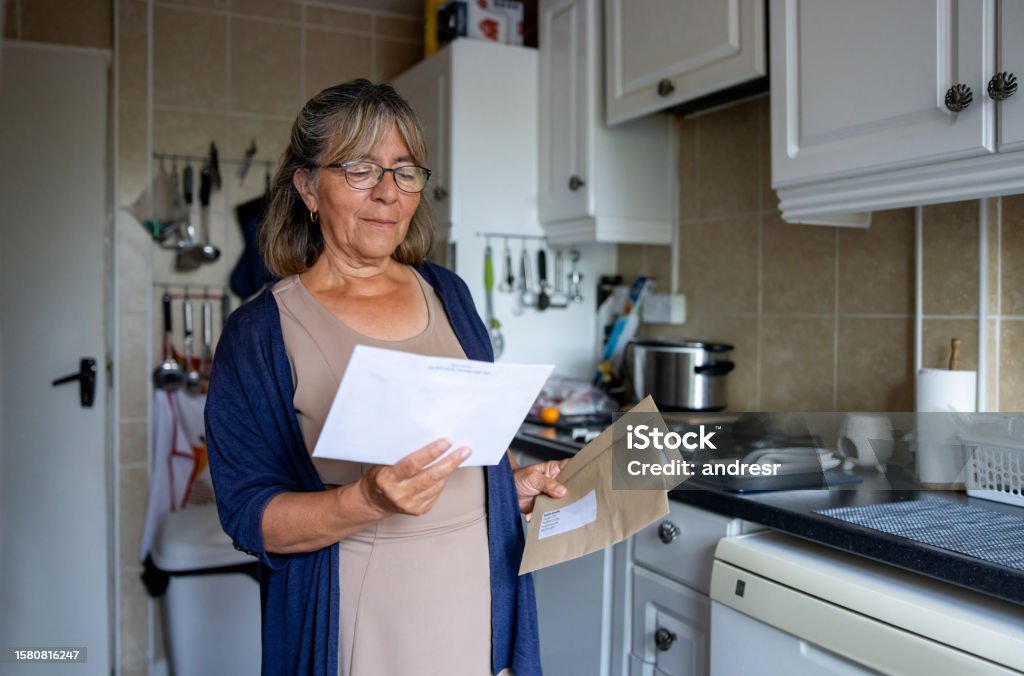 Senior woman at home checking her mail Portrait of a senior woman at home checking a letter in the mail - domestic life concepts Letter - Document Stock Photo