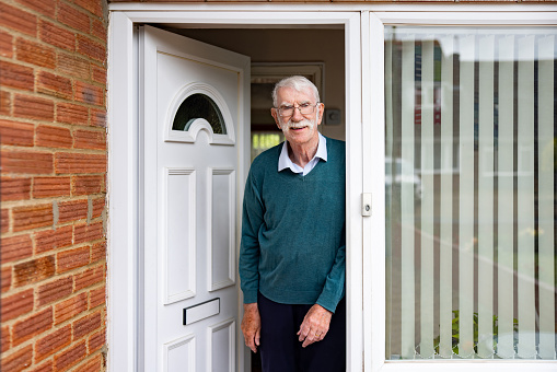 Happy mature man standing at the front door of his house and looking at the camera smiling