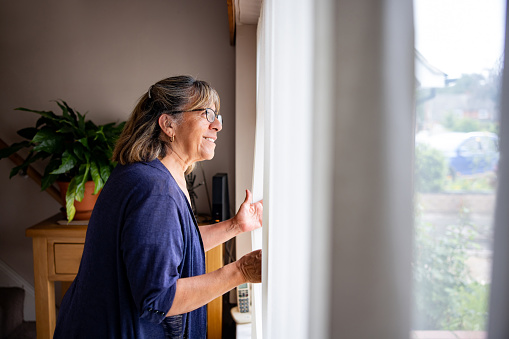 Nosy senior woman at home looking at her neighbors through the window - retirement concepts