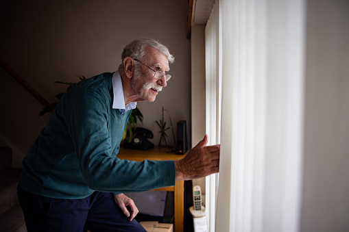 Nosy senior man at home looking through the window at his neighbors -domestic life concepts