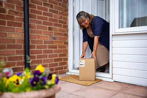 Mature woman at home receiving a package in the mail and picking it up at the front door - post service concepts