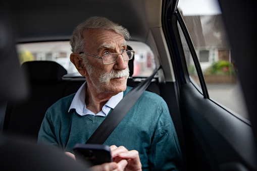 Senior adult riding on a crowdsourced taxi and using his cell phone and looking through the window