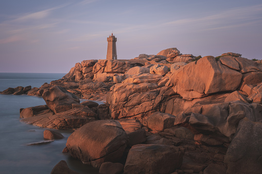 Moments before sunrise at Portland Head Lighthouse, Portland, Maine. Shot form the north towards lighthouse and light keeper's house on cliffs. Fiery  orange clouds at horizon with blue sky above.