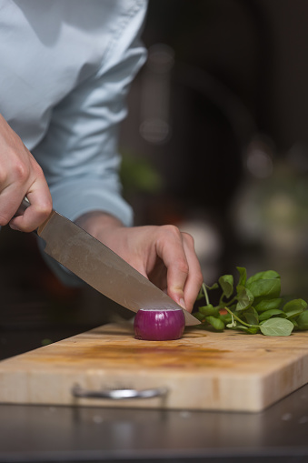 Chef cutting red onion down the middle, prepairing healthy food on a wooden cutting board. Preparing healthy meal at home.