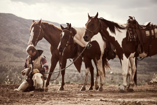 cowboy kneeling in prayer with his horses behind