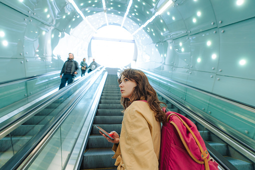 Young woman with backpack  using smartphone on the escalator