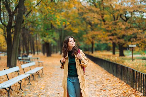 Young  woman with backpack walking in the park in autumn and enjoying serenity