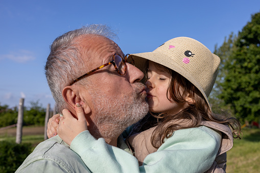 Little happy daughter kisses her grey haired father outside