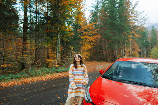 Cheerful woman standing near the car in the forest in autumn