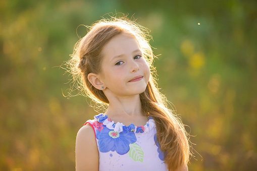 Close-up portrait of a charming blonde girl in the rays of the setting sun