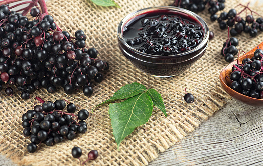 Alternative medicine - Fresh ripe black elderberries, elderberry syrup and leaves of elderberry on rustic wooden boards background.