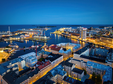 Helsinki Cityscape illuminated at Night. Aerial Drone Point of View Stitched Night, Twilight Panorama. Aerial view from the district of Kamppi towards the Waterfront of Jätkäsaari District and Munkholmen with beautiful illuminated buildings towards the harbour and Baltic Sea. Helsinki, Finland, Nordic Countries, Northern Europe.