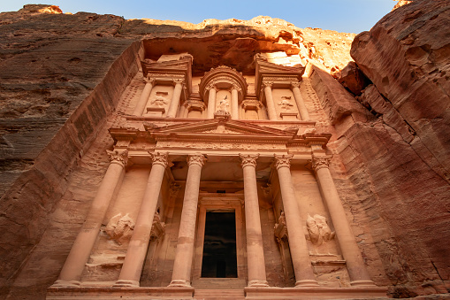 View of the Al-Khazneh Palace or Treasury in Petra, Jordan. The building is carved into a huge rock, has an elegant pediment and towering columns.