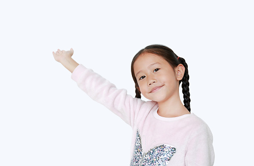 Smiling little Asian child girl standing and pointing up present something isolated over white background. Asian schoolgirl in education concept.
