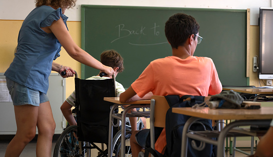 A teacher assists a disabled student with a wheelchair. Back to school concept