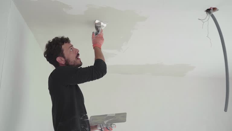 Man at work plastering ceiling in indoor construction site