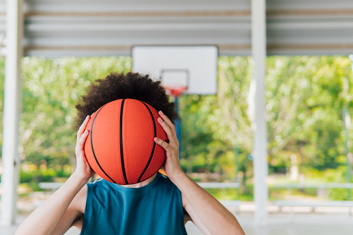 Photo with copy space of a young basketball player hiding his face with a basketball