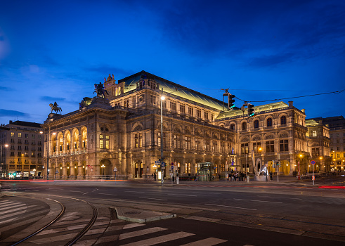 Vienna, AUSTRIA - May 25, 2023: Illuminated Vienna Opera House during blue hour / twilight. People unidentifiable due to motion blur. Light streaks caused by tramways and cars passing.