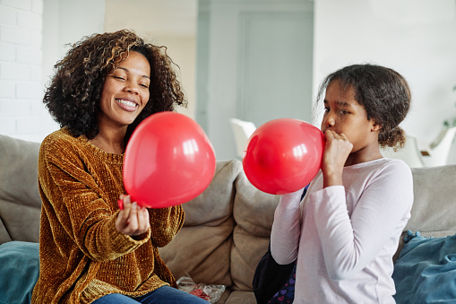 mother and teen daughter playing and having fun blowing balloons at home