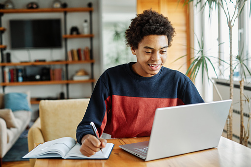 Portrait of teenage black boy using laptop computer at home. Teenage boy attending to online school class