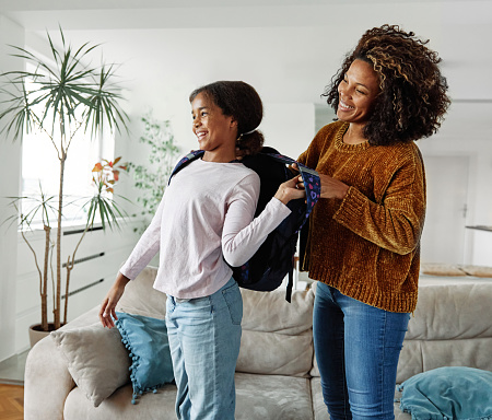 Mother helping daughter to get ready for school, helping her with backpack and books,hugging and leaving home