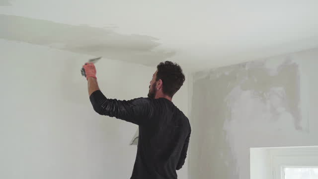 Working man plastering white surface in indoor home construction site