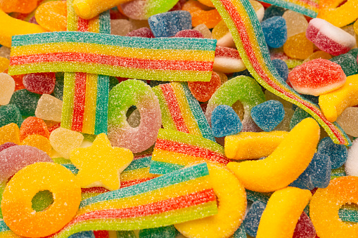 Top view of an assortment of multicolored candies, lollipops and jelly beans background. All the candies are at the center of the image making a horizontal stripe shape and leaving a useful copy space at the top and at the lower side of the image on a withe background.  Studio shot taken with Canon EOS 6D Mark II and Canon EF 24-105 mm f/4L