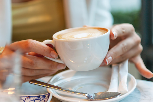 Close-up of a woman holds a cup full of coffee in a restaurant or cafe above a saucer with sugar sachets and a teaspoon