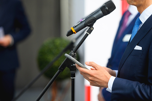 Businessman or politician checks data on a smart phone before the start of a public event. He stands with the phone in his hands in front of the microphone stand, copy space