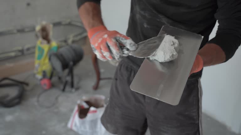 Professional builder man working and preparing plaster for indoor drywalls, hands and tools detail