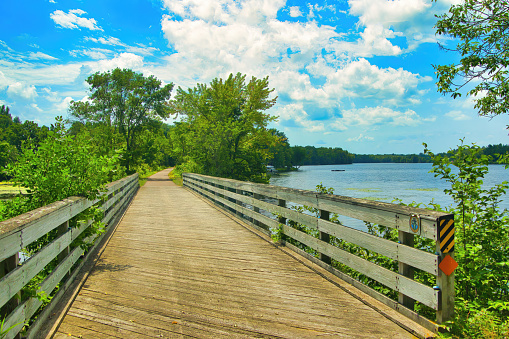 As seen on a beautiful Summer day, a wooden bridge along the Old Abe State Trail passes by the Chippewa River near Jump River, WI.