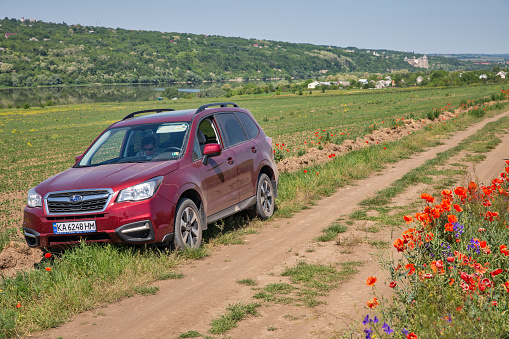 Khotyn, Ukraine - June 01, 2023: Red SUV Subaru Forester in front of Dnister river and Fortress Subaru Forester is a compact crossover that has been manufactured by Subaru since 1997.