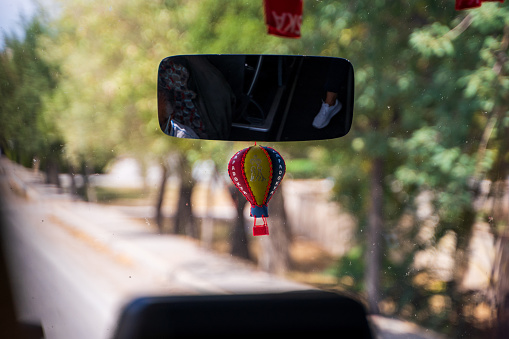 A rear mirror in a bus with a hanging air balloon during a journey signifying destination as cappadocia