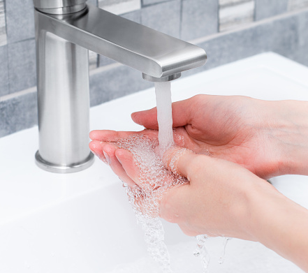 a woman washes her hands with a jet of water from a tap in the bathroom, close-up