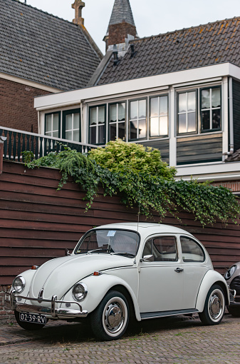 Enkhuizen, the Netherlands - July 29th 2023: A pristine white 1971 Volkswagen Beetle parked besides a beautiful 1930's house.