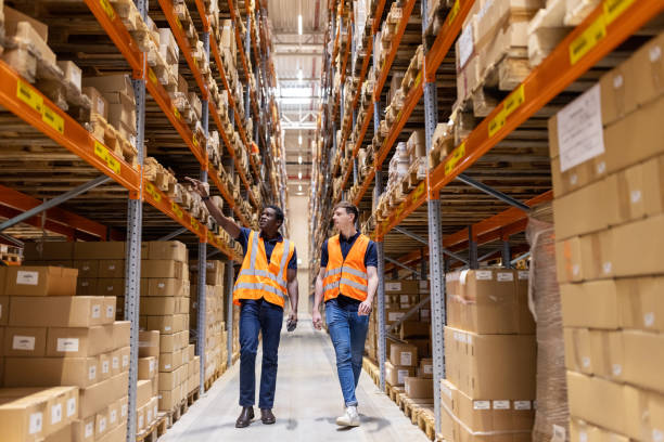 istock Two male employees discussing while walking through warehouse aisle 1581299864