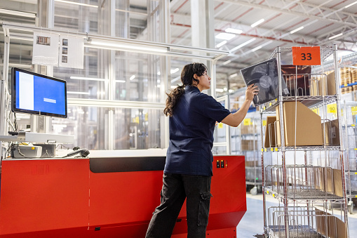 Young woman placing a delivery box on rack while working at warehouse. Female employee preparing parcel for delivery at warehouse.